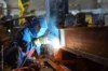 Welder wearing protective gear working on a metal structure, with sparks flying around.