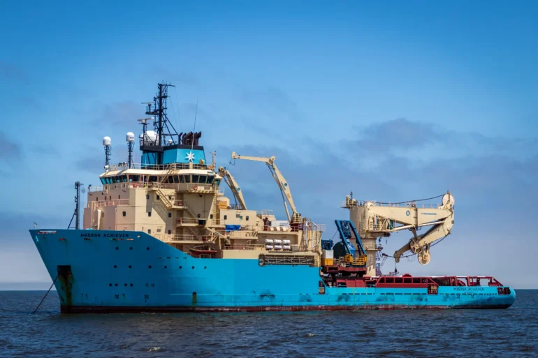 Blue offshore vessel equipped with cranes and machinery, floating on the water.