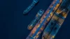 Aerial view of ships docked at a port during nighttime, illuminated by lights.