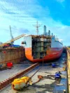 A large ship in a dry dock undergoing maintenance or construction, with visible chains and equipment in the foreground.