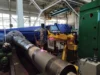 Industrial machine in a factory setting, working on a large metal cylinder.