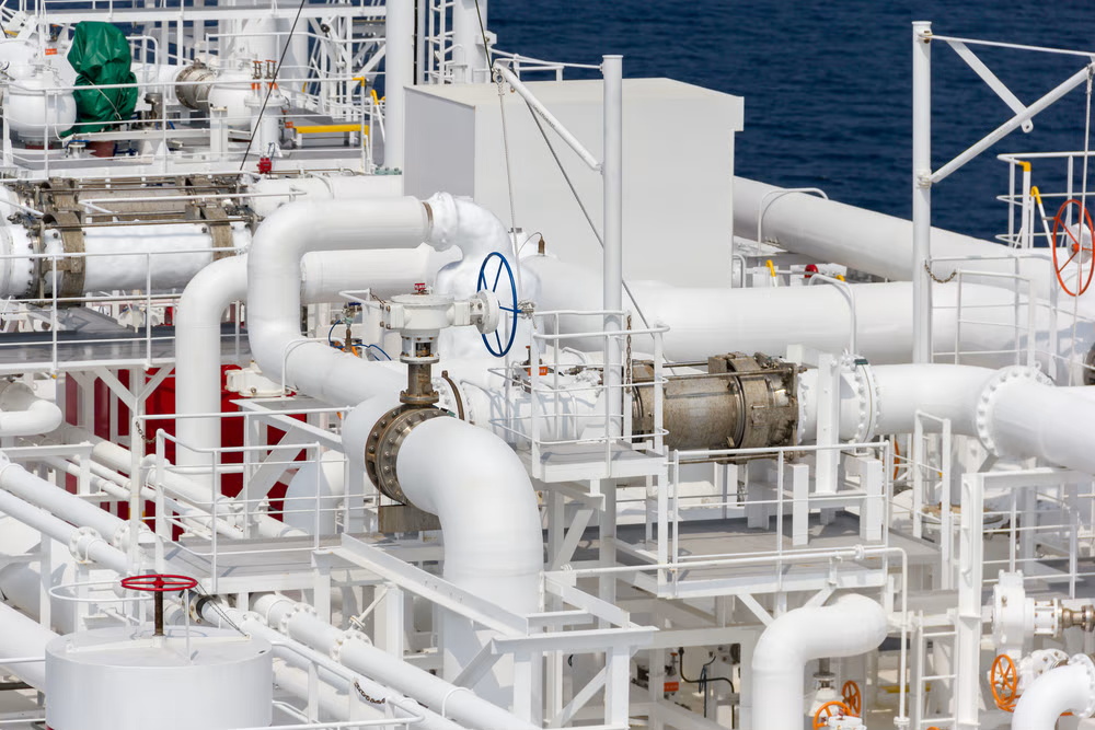 Complex network of white industrial pipes and valves on a maritime vessel.